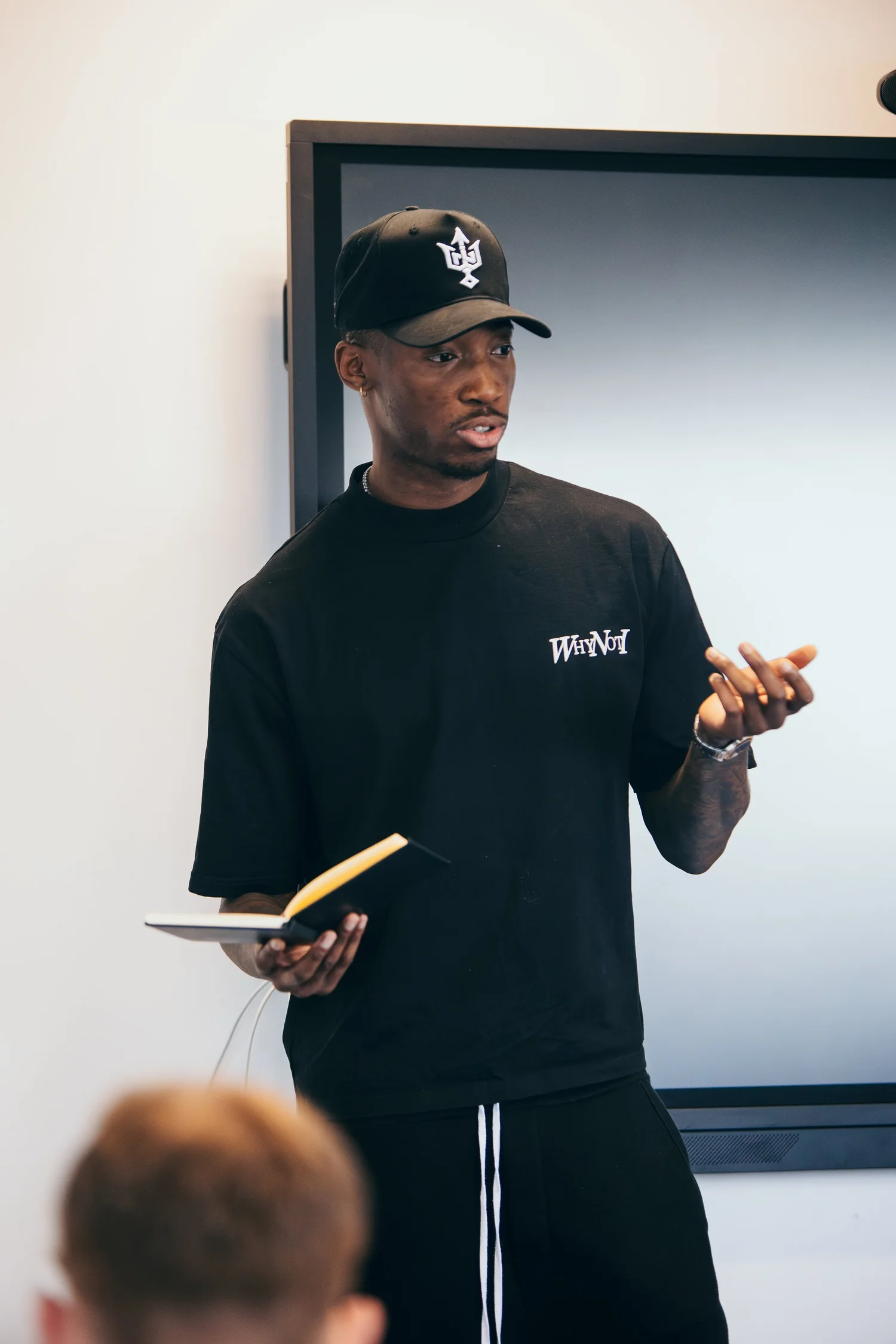 Kofi speaking to participants while holding a Why Not I booklet during the 2024 Workout