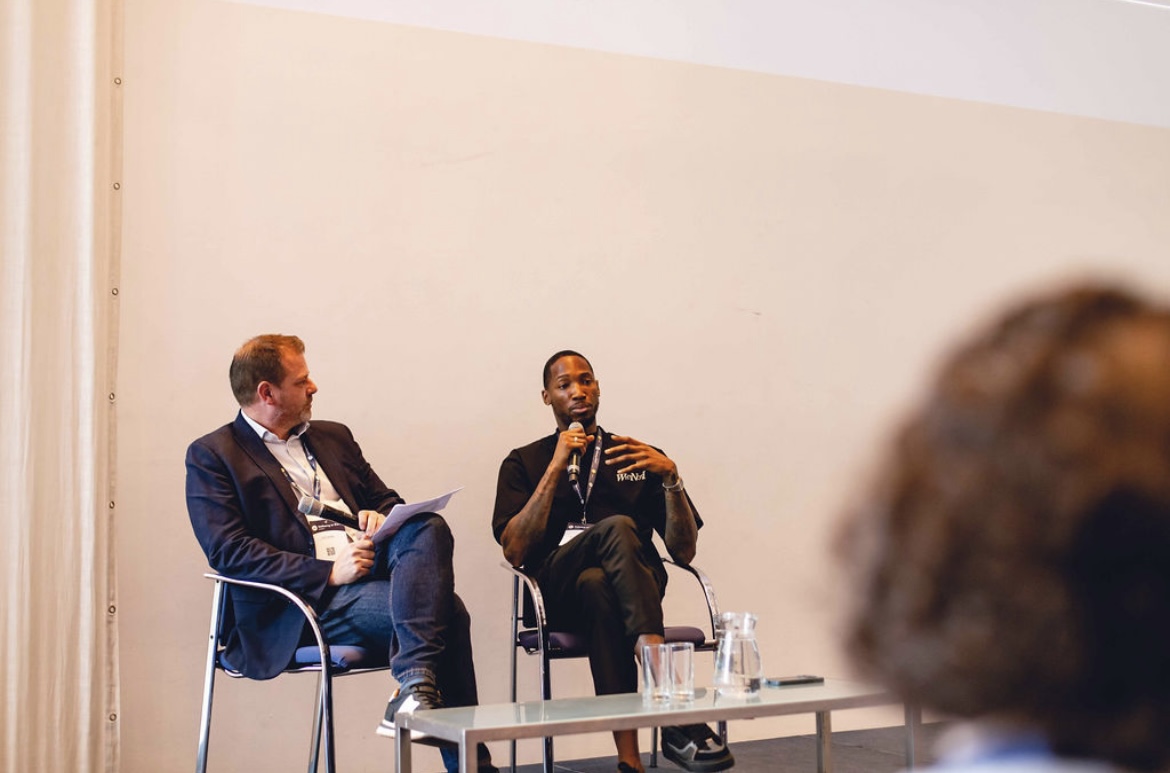 Kofi Josephs in conversation on stage with the host of a workplace wellbeing summit